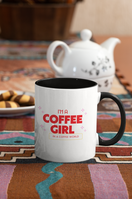 White mug with black handle and red text 'I'm a Coffee Girl in a Coffee World' on a colorful tablecloth.